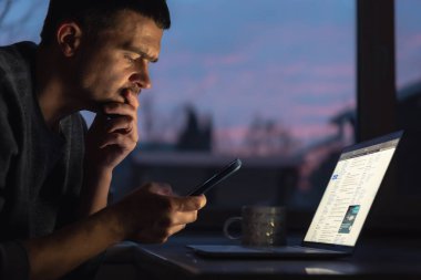 Sabahın köründe, sabahın köründe bir bilgisayarın arkasında akıllı bir telefonla çalışan bir adam..