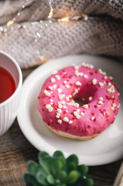 Pembe bir donut, bir fincan çay ve örgü elementi ile rahat bir kompozisyon..