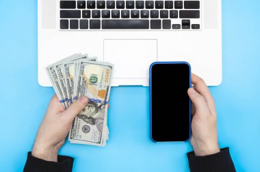 Laptop, akıllı telefon ve para erkeklerin elinde mavi bir arka plan, üst görünüm.