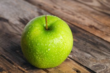 Ahşap arka planda su damlaları olan yeşil taze elma..
