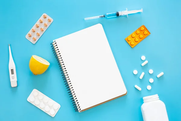 Blank notepad, medicines, pills and thermometer on a blue background, flat lay, copy space.