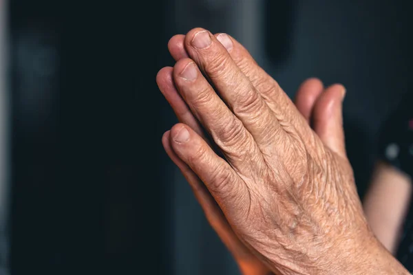 Hands of an old woman folded for prayer on blurred background, the concept of faith in God and religiosity.