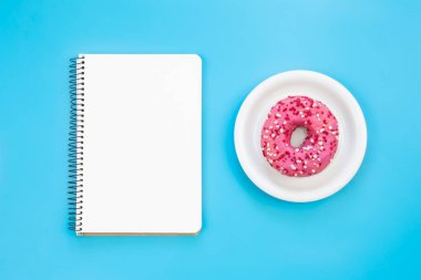 Mavi arkaplanda boş not defteri ve çörek, düz konum, kopyalama alanı.