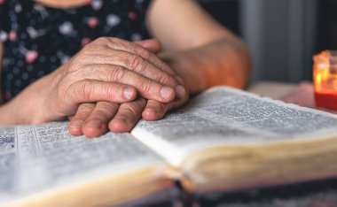 Yaşlı bir kadın incili okuyor, buruşuk eller yakın..
