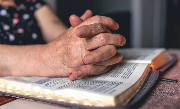 An old woman reads the Bible, wrinkled hands close up.