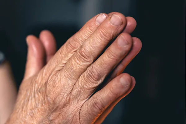 Hands of an old woman folded for prayer on blurred background, the concept of faith in God and religiosity.