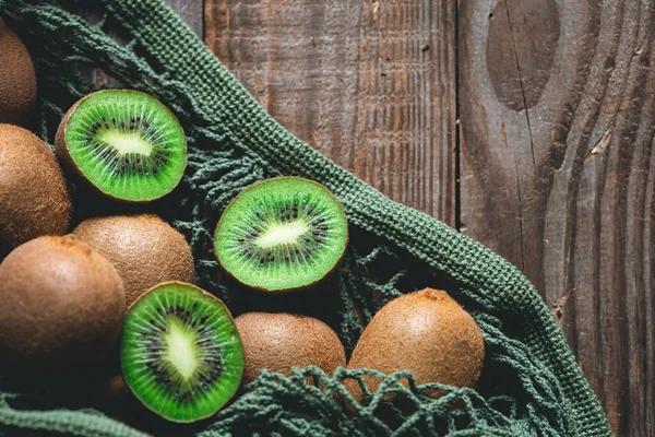 Kiwi fruits in a mesh bag on a wooden background, top view, rural style, eco concept.