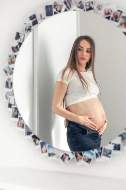 Attractive young pregnant woman in mirror reflection at home, concept of expecting a baby and womens health.