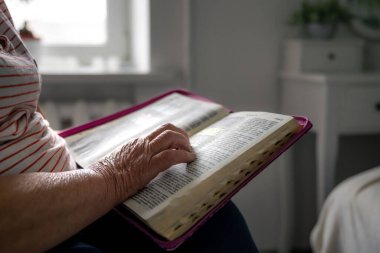 Yaşlı bir kadın evde İncil okuyor, buruşuk eller yakın, boşluğu kopyalıyor..
