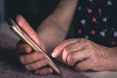 Elinde cep telefonu olan yaşlı bir kadının elleri..