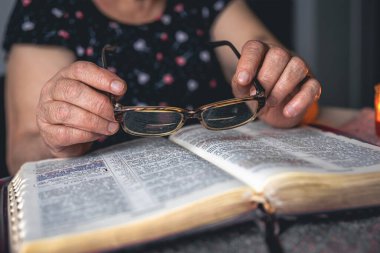 Yaşlı bir kadın İncil okuyor ve elinde bardaklar, elleri kapalı..