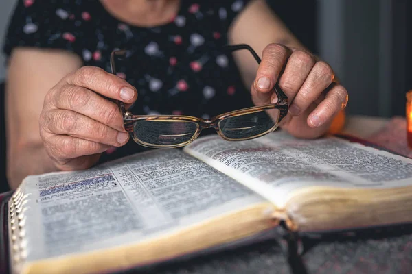 Yaşlı bir kadın İncil okuyor ve elinde bardaklar, elleri kapalı..