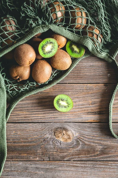 Kiwi fruits in a mesh bag on a wooden background, top view, rural style, eco concept.