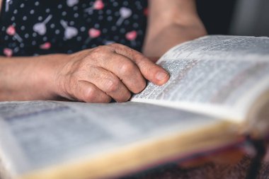 Yaşlı bir kadın incili okuyor, buruşuk eller yakın..