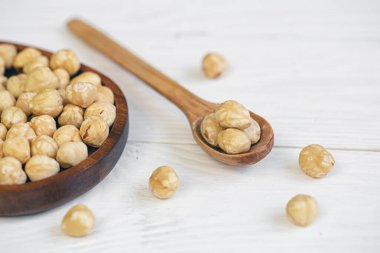 Peeled hazelnuts in a wooden spoon on a white wooden background, close-up.