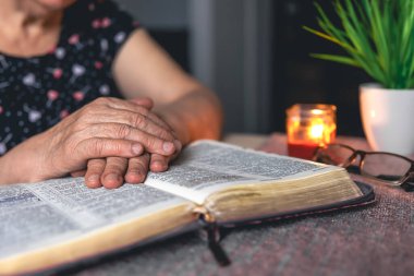 Yaşlı bir kadın incili okuyor, buruşuk eller yakın..