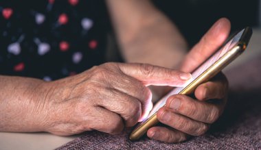 Elinde cep telefonu olan yaşlı bir kadının elleri..