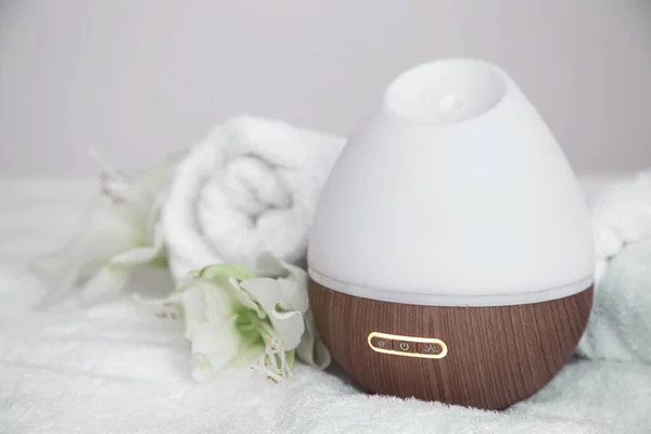 Modern oil aroma diffuser, and lily flowers on blurred background. The concept of refreshing and purifying the air in the house.