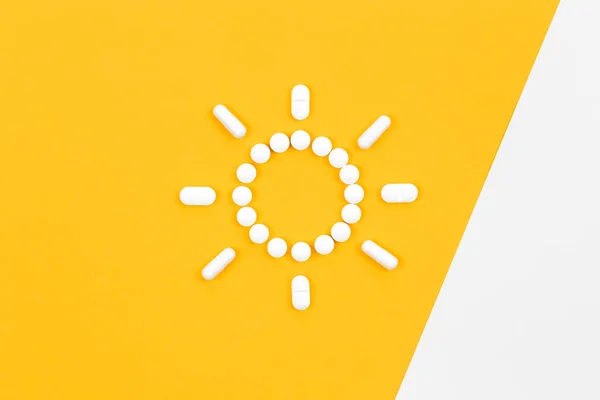Pills in the shape of the sun, on a yellow background, flat lay, the concept of health, vitamins and vitamin D.