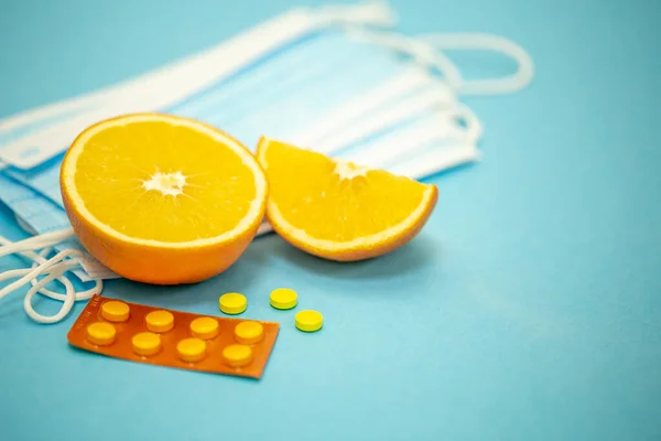 Orange fruit, pills and masks on a blue background, disease prevention concept.