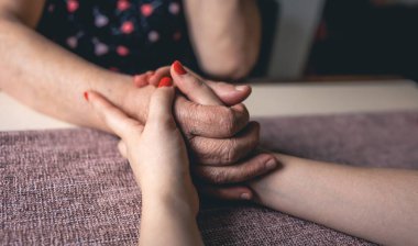 Yaşlı ve genç kadınların el ele tutuşması, yaşlı bakımı ve saygısı, yakın çekim.