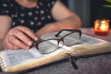 Yaşlı bir kadın İncil okuyor ve elinde bardaklar, elleri kapalı..