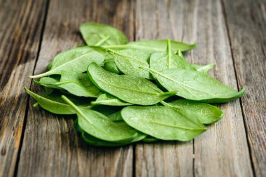 Wet fresh green baby spinach leaves on a wooden background, close up.