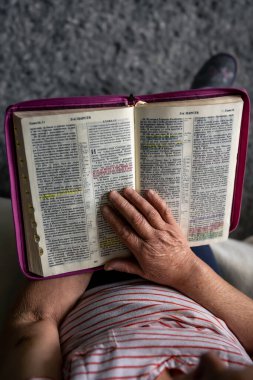 An old woman reads the Bible at home, wrinkled hands close up, top view.