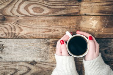 Female hands with red manicure, holding a cup of coffee on a wooden background, flat lay, copy space.