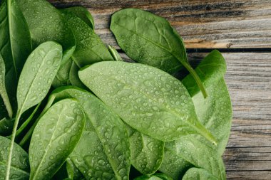 Wet fresh green baby spinach leaves on a wooden background, top view.