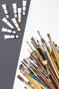 Paint brushes of different sizes and paints in tubes on a paper colored background, flat lay.