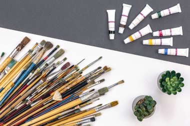 Paint brushes of different sizes and paints in tubes on a paper colored background, flat lay.