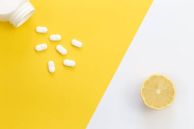 Sarı arka planda haplar ve limon, düz yatak, C vitamini konsepti.