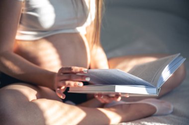 A pregnant woman reading a book at her home, close up.