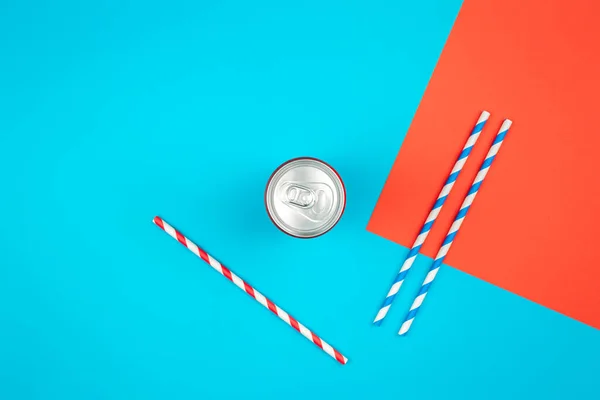 Aluminum drink or beverage can with pull ring on colored background with colored paper straws, flat lay.