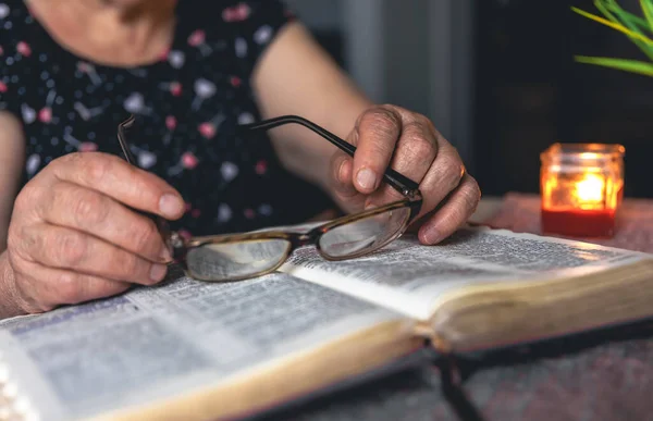An old woman reads the Bible and holding glasses, hands close up.