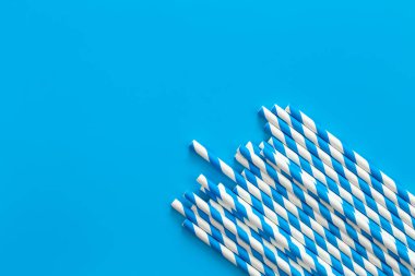 Drinking straws for party on blue background. Top view of blue paper disposable, eco-friendly straws for summer cocktails, copy space.