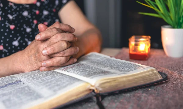 Yaşlı bir kadın incili okuyor, buruşuk eller yakın..
