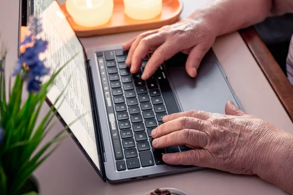 An old woman uses a laptop, reads news on the Internet, close-up hands, the concept of technology and old people.
