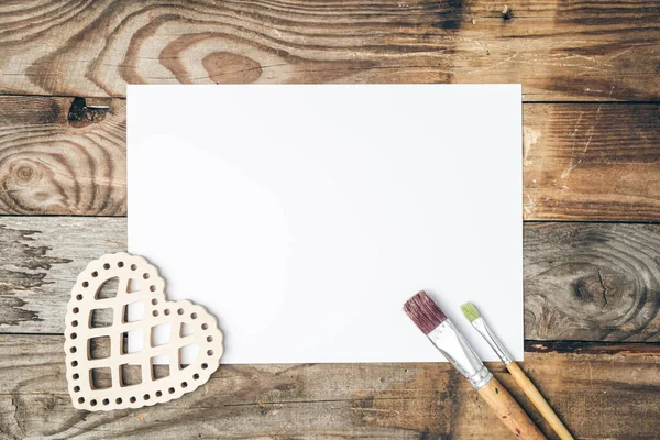 Blank sheet of paper and brushes for drawing on a wooden background, flat lay, copy space.