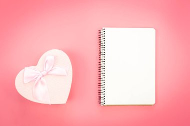Blank notebook and heart shaped gift box on pink background, top view, copy space.