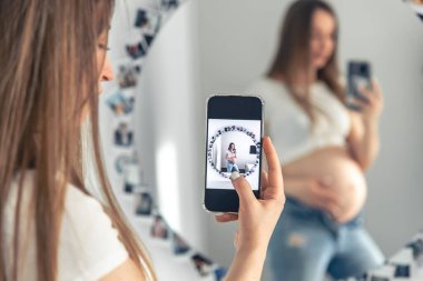 A pregnant woman takes a selfie on a smartphone in the mirror, the concept of expecting a baby.