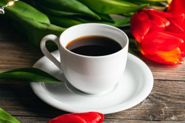 Spring composition with a cup of coffee and red tulips on a wooden surface, close up.