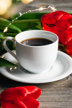 Spring composition with a cup of coffee and red tulips on a wooden surface, close up.