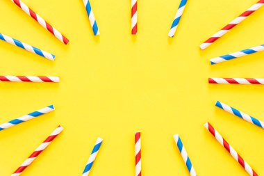 Multicolored party drinking straws arranged into a circle on yellow background, top view, copy space.