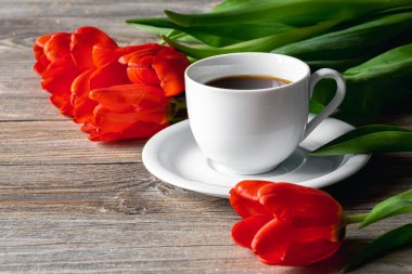 Spring composition with a cup of coffee and red tulips on a wooden surface.