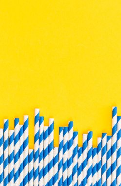 Drinking straws for party on yellow background, copy space. Top view of blue paper disposable, eco-friendly straws for summer cocktails.