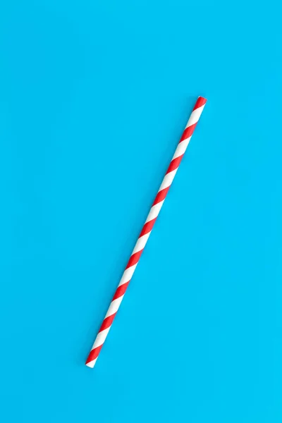 Close up of drinking straw for party, red spiral. Top view of colorful disposable eco-friendly straw for summer cocktails. Paper cocktail colorful straw isolated on blue background, isolated.