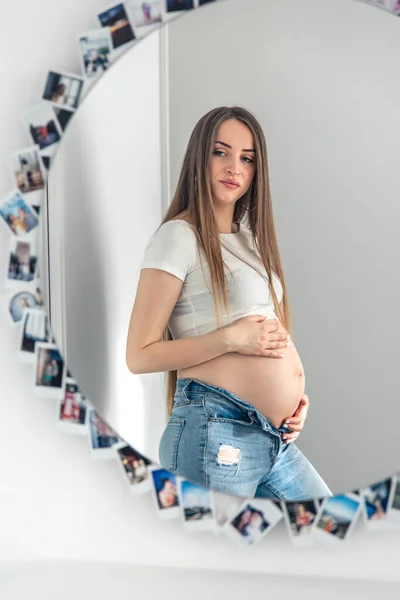 Attractive young pregnant woman in mirror reflection at home, concept of expecting a baby and womens health.