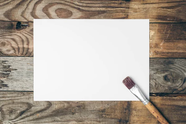 Blank sheet of paper and brush for drawing on a wooden background, flat lay, copy space.
